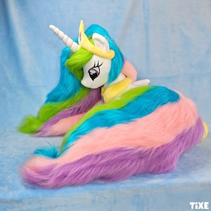 May include: A plush toy of a white unicorn with a long, flowing mane and tail in shades of blue, green, pink, and purple. The unicorn has a white horn, a yellow crown, and large, expressive eyes. The toy is made of soft, plush material.