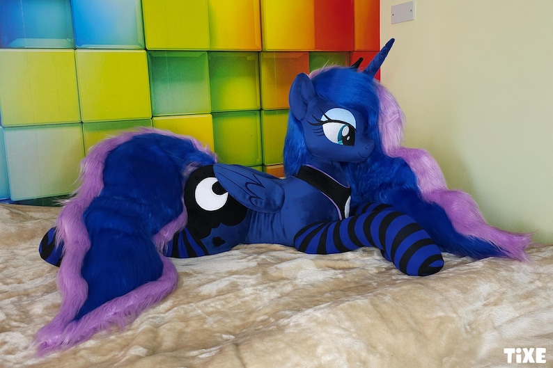 May include: A plush toy of Princess Luna from My Little Pony. The toy is primarily blue with a purple mane and tail. It has a black and white crescent moon symbol on its flank and black and blue striped legs.