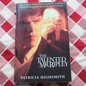 May include: A book cover with a photo of Matt Damon on the front. The title of the book is "The Talented Mr. Ripley" by Patricia Highsmith.