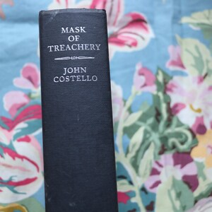 May include: A black hardcover book with the title "Mask of Treachery" and the author's name "John Costello" printed in white on the spine.