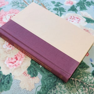 May include: A closed book with a cream colored cover and a maroon spine. The title of the book is "The Most Beautiful Heart in the World" by W.E.B. Griffin.