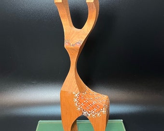 Könnte beinhalten: Eine Holzfigur eines Rentiers mit einem stilisierten Design. Das Rentier ist in Braun- und Orangetönen mit weißen und roten Details bemalt. Das Rentier steht auf einem grünen Buch.