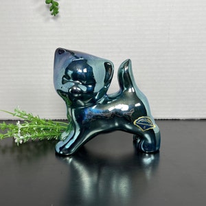 May include: A blue iridescent ceramic figurine of a cat. The cat is standing on all fours with its tail raised. The figurine has a shiny, metallic finish.
