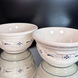 Puede incluir: Dos cuencos de cerámica de color crema con una textura en relieve de tejido de cesta en el exterior. Cada cuenco está decorado con pequeños detalles florales azul oscuro y patrones de líneas curvas espaciados uniformemente en el exterior.