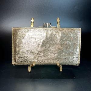 Cartera Baronet Fifth Avenue de lamé dorado metalizado con dos bolsillos centrales y cierre de doble beso, broches a presión en ambos lados, estilo vintage de los años 60