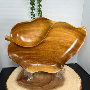 May include: A wooden serving dish shaped like a leaf with two separate compartments. The dish is made of light brown wood and has a natural, polished finish.