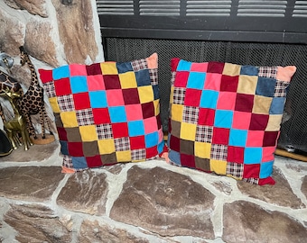 Könnte beinhalten: Zwei quadratische Patchwork-Kissen in verschiedenen Farben wie Rot, Blau, Gelb, Braun und Rosa. Die Kissen sind aus verschiedenen Stoffen gefertigt und haben eine gesteppte Optik.