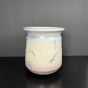 May include: A white ceramic vase with a blue and pink floral design. The vase has a rounded bottom and a wide mouth.