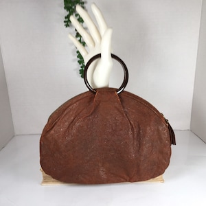 May include: A brown leather handbag with a large, round wooden handle. The bag has a slightly rounded, dome-like shape.