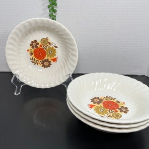 May include: Set of four white ceramic bowls with a swirling design. Each bowl features a floral pattern with orange, brown, and green flowers.