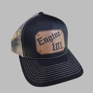 May include: Black and gray trucker hat with a brown leather patch that says "Engine 101" in a gothic font.
