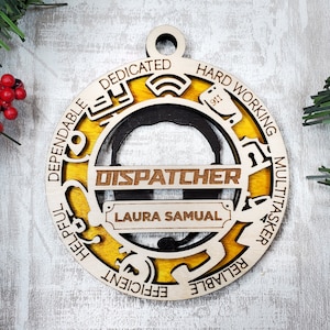 May include: A wooden Christmas ornament with a yellow background and a black silhouette of a dispatcher's headset. The ornament is inscribed with the words "Dispatcher", "Laura Samual", "Dependable", "Dedicated", "Hard Working", "Multitasker", "Helpful", "Efficient", "Reliable".