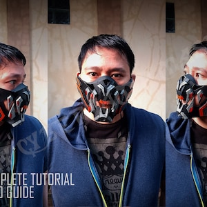 May include: A person wearing a black and orange 3D printed mask with a geometric design. The mask has a mouth opening and is attached to a black strap. The person is wearing a blue hoodie and a black t-shirt. The image includes the text "PDF FILE WITH COMPLETE TUTORIAL AND VIDEO GUIDE".