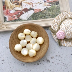 May include: A wooden bowl filled with white mother of pearl buttons. The buttons are round and have a slight iridescent sheen.