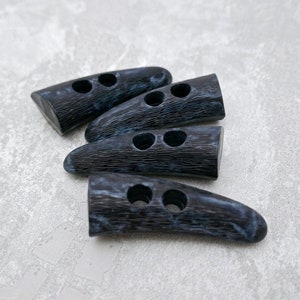 May include: Four black and blue plastic toggle buttons with two holes each. The buttons are shaped like a horn and have a textured surface.