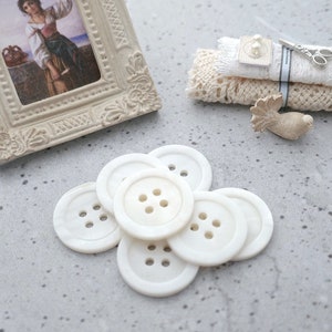 May include: A group of six white, round buttons with four holes each. The buttons are arranged in a circle, with the largest button in the center.