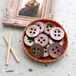 May include: A small wicker basket filled with a variety of brown and iridescent buttons. The buttons have four holes each and are arranged in a random pattern.
