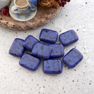May include: A group of ten small, rectangular, blue glass tiles with a marbled pattern. The tiles are scattered on a light gray surface.
