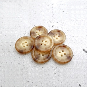 May include: Six brown and cream mottled buttons with four holes each. The buttons are arranged in a loose pile.