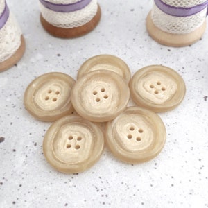 May include: Six beige buttons with four holes each. The buttons have a textured, slightly raised design.