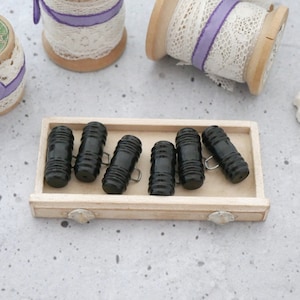 May include: A wooden box filled with six black, ribbed, plastic buttons. The buttons have a metal loop on the side.