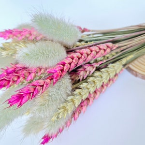 May include: A bouquet of dried flowers with pink wheat, beige wheat, and white fluffy bunny tail grass.