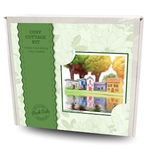 May include: A white box with a green panel displaying "COSY COTTAGE KIT" and "Make 5 air-drying clay models." The box shows a miniature village scene with colorful houses reflected in water. The text "Led tealights included" is also printed on the box.