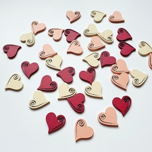 Puede incluir: Una colección de adornos de madera en forma de corazón en varios tonos de rosa, rojo y crema. Cada corazón presenta un diseño de espiral decorativo.