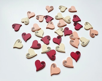 May include: A collection of wooden heart-shaped ornaments in various shades of pink, red, and cream. Each heart features a decorative swirl design.