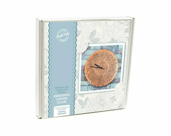 May include: A craft kit for an embossed copper clock, presented in a box. The clock face features a detailed, circular design with a copper finish. The box has a floral pattern and the text "Embossed Copper Clock."