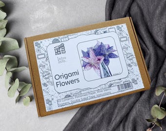 Puede incluir: Una caja marrón con una etiqueta blanca que dice "Origami Flowers" e incluye una imagen de un ramo de flores de origami. El kit contiene papel estampado, tallos de alambre, estambres, cinta adhesiva de doble cara e instrucciones.