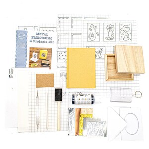 metal embossing starter kit laid out with aluminium, copper, gold foil, and pewter sheets, wooden box, A6 notebook, card and envelope, key fob, embossing tools, paints, tracing paper, and instruction booklet, Flat lay of a metal embossing craft kit including pre-cut aluminium, copper, gold foil, and pewter sheets, a small wooden box, A6 notebook, greeting card with envelope, plastic key ring, embossing tool, foam brush, sandpaper, tracing paper, adhesive sheet, and full-colour instructions