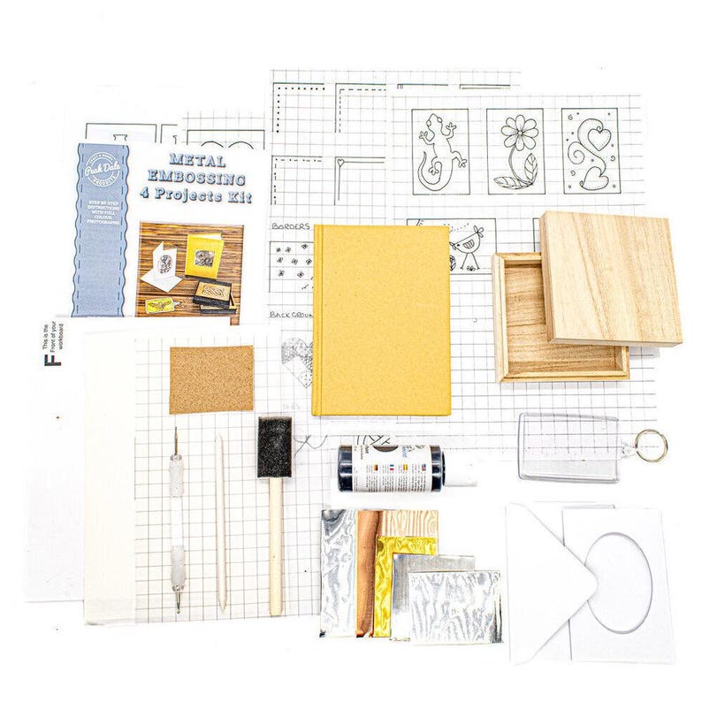 metal embossing starter kit laid out with aluminium, copper, gold foil, and pewter sheets, wooden box, A6 notebook, card and envelope, key fob, embossing tools, paints, tracing paper, and instruction booklet, Flat lay of a metal embossing craft kit including pre-cut aluminium, copper, gold foil, and pewter sheets, a small wooden box, A6 notebook, greeting card with envelope, plastic key ring, embossing tool, foam brush, sandpaper, tracing paper, adhesive sheet, and full-colour instructions