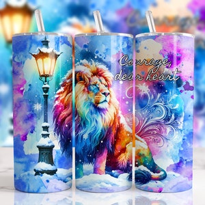 Könnte beinhalten: Drei Edelstahlbecher mit bunten Aquarelldesigns. Der erste Becher zeigt eine Straßenlaterne mit Schnee auf dem Boden. Der zweite Becher zeigt einen bunten Löwen mit Schnee auf dem Boden. Der dritte Becher zeigt einen bunten Löwen mit dem Text "Mut, liebes Herz".