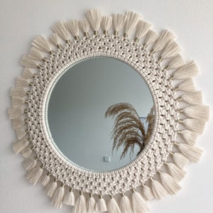 May include: A round mirror with a macrame frame and white tassels. The mirror has a gold trim around the edge.