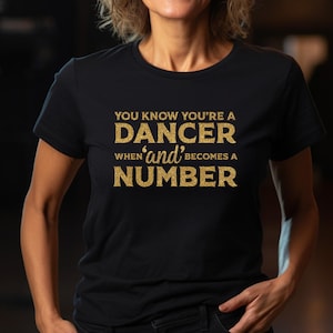 May include: Black t-shirt with gold glitter text that reads "You know you're a dancer when 'and' becomes a number."