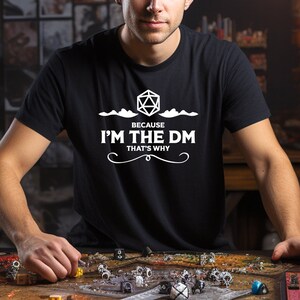 May include: A black t-shirt with a white graphic design featuring a 20-sided die, clouds, and the text "Because I'm the DM That's Why".