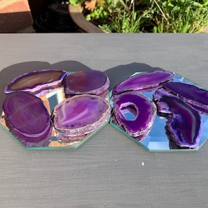 May include: Set of purple agate coasters with natural patterns and edges. The coasters are displayed on a mirrored surface.