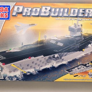 May include: A Mega Bloks ProBuilder Master Series USS Nimitz model kit. The box art shows a detailed aircraft carrier with planes, set against a sea and sky backdrop. The kit includes 1400 pieces and is for ages 10 and up.