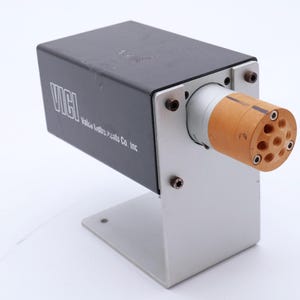 May include: A rectangular black metal device with the text "VICI" and "Value Electric Products Co. Inc." in white. It has a cylindrical wooden component with multiple holes and is mounted on a silver metal base.