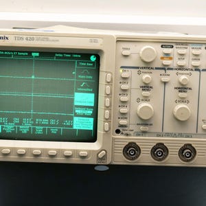 May include: A Tektronix TDS 420 oscilloscope with a green display showing waveforms. The device has numerous buttons and knobs for vertical, horizontal, and trigger adjustments. The screen displays text and a grid pattern.