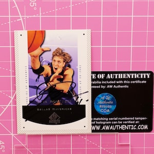 Puede incluir: Una tarjeta de baloncesto con un jugador sosteniendo un balón. La tarjeta presenta un autógrafo y el logotipo de los Dallas Mavericks. Incluye un certificado de autenticidad de AW Authentic.