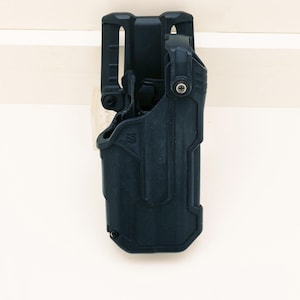 May include: A black, molded polymer holster with a belt loop and retention features. The holster is designed to securely hold a firearm. The design includes a textured surface and various attachment points. The holster is shown against a white background.
