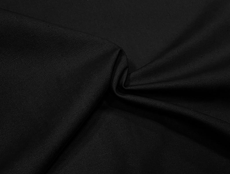 May include: Black fabric with a smooth, textured surface. The fabric is folded and draped, creating soft folds and curves.