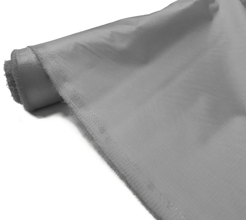 May include: A roll of light gray fabric with a subtle texture. The fabric has a finished edge.