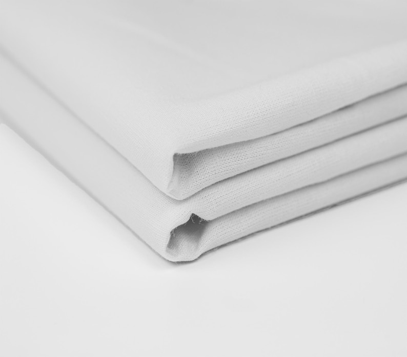 May include: A stack of three white fabric napkins folded neatly.