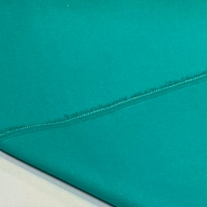 K&ouml;nnte beinhalten: Nahaufnahme eines t&uuml;rkisfarbenen Stoffes mit einer rohen Kante und einer Naht, die diagonal &uuml;ber den Stoff verl&auml;uft.