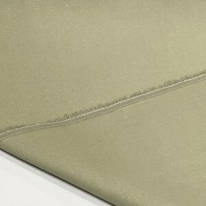 May include: A close-up of a piece of light brown fabric with a raw edge and a seam running diagonally across it.