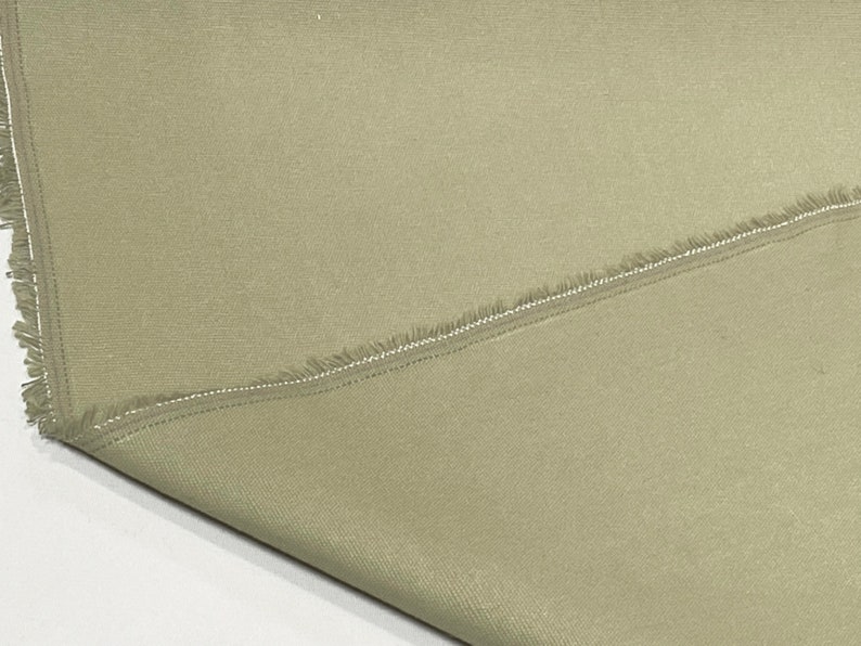May include: A close-up of a piece of light brown fabric with a raw edge and a seam running diagonally across it.