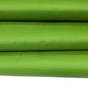 May include: Close-up of a green fabric with a grid pattern. The fabric is folded in thirds, showing the texture and weave.